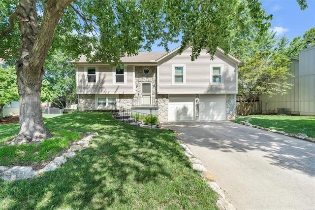 raised ranch featuring fence, a garage, stone siding, driveway, and a front lawn