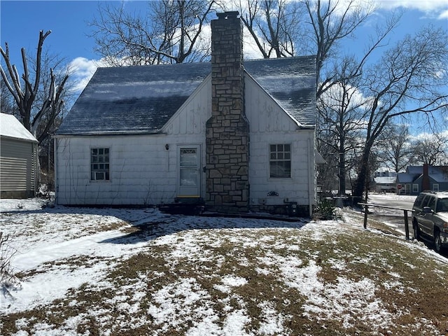 snow covered rear of property featuring roof with shingles and a chimney