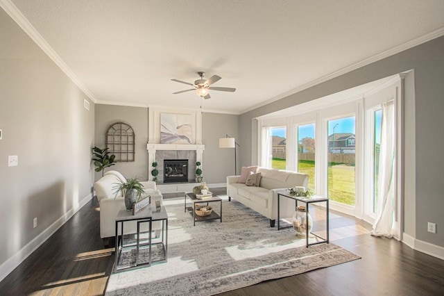 living room with wood finished floors, a ceiling fan, baseboards, ornamental molding, and a tiled fireplace