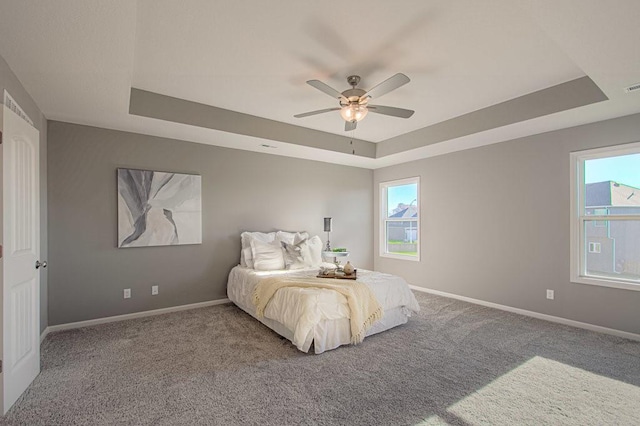 carpeted bedroom featuring a ceiling fan, a tray ceiling, visible vents, and baseboards