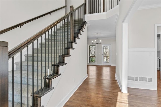 foyer featuring baseboards, visible vents, ornamental molding, wood finished floors, and a chandelier