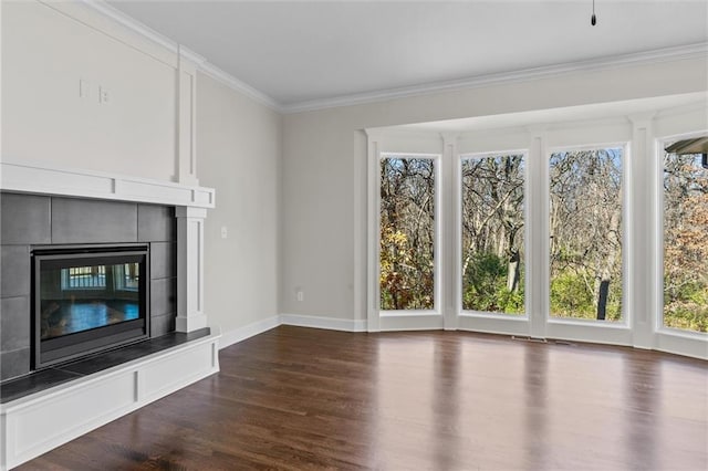 unfurnished living room featuring crown molding, plenty of natural light, a tiled fireplace, and wood finished floors