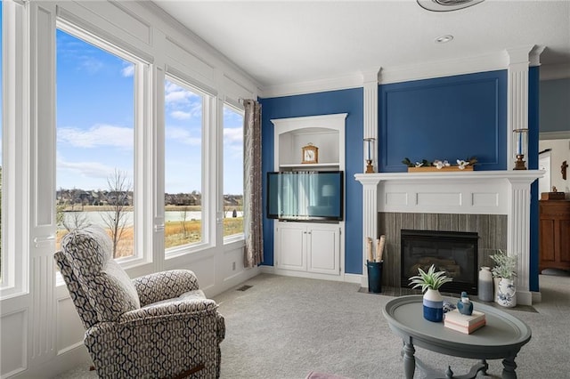 living area featuring visible vents, a decorative wall, ornamental molding, a brick fireplace, and light carpet