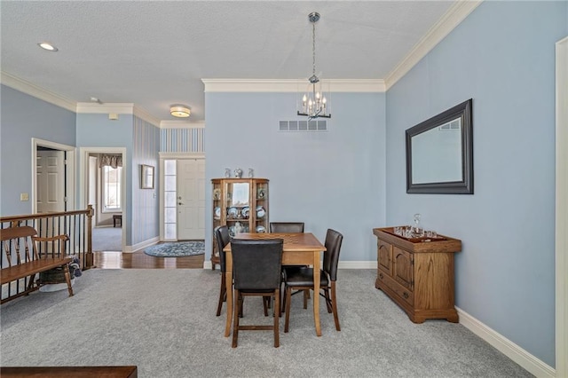 carpeted dining space featuring baseboards, visible vents, a chandelier, and crown molding