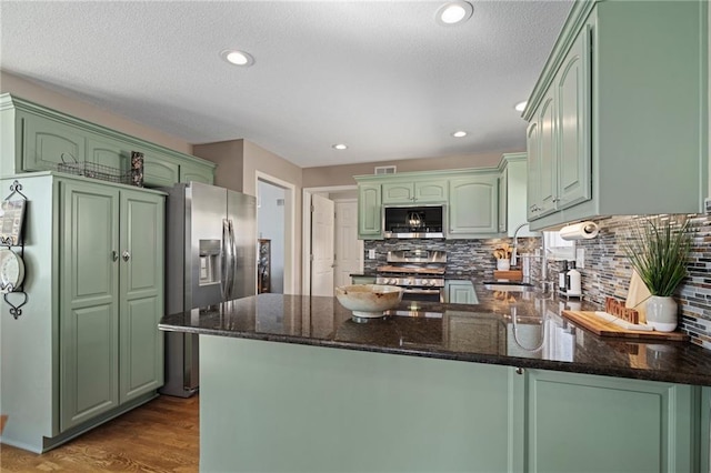 kitchen with wood finished floors, a peninsula, a sink, stainless steel appliances, and green cabinetry