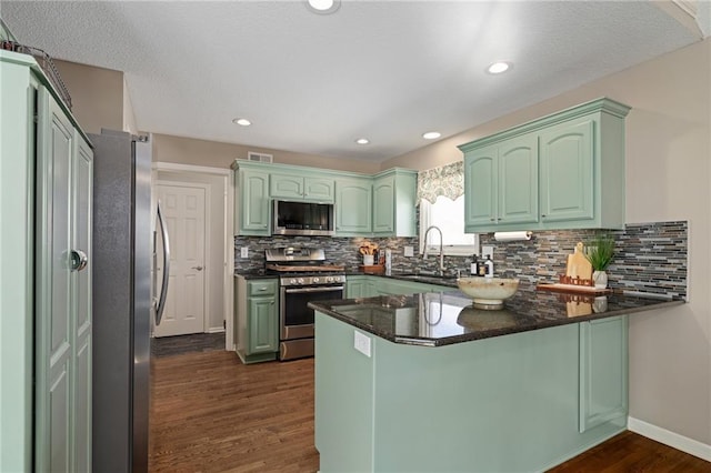 kitchen with a peninsula, appliances with stainless steel finishes, green cabinets, and a sink