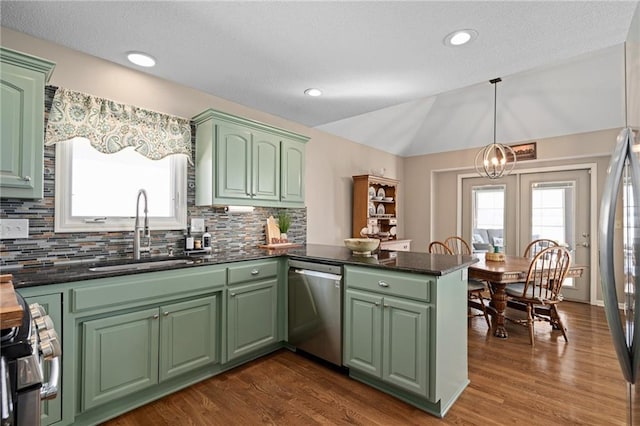 kitchen with lofted ceiling, appliances with stainless steel finishes, a peninsula, a sink, and green cabinetry