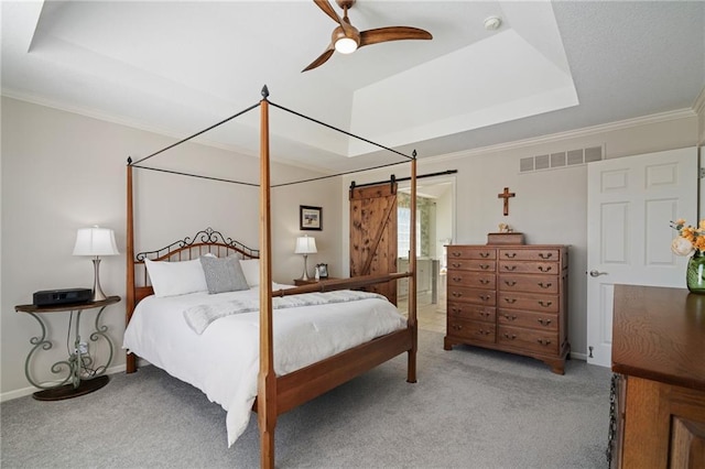 bedroom with carpet floors, a tray ceiling, a barn door, and visible vents