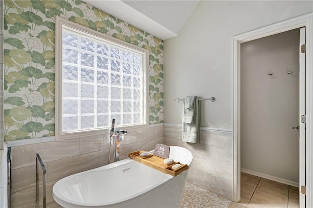 bathroom with tile walls, wainscoting, a textured ceiling, tile patterned flooring, and a freestanding tub