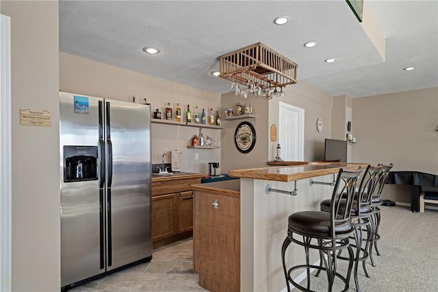 kitchen featuring stainless steel fridge with ice dispenser, a kitchen breakfast bar, brown cabinets, a textured ceiling, and a sink