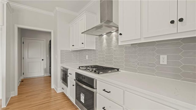kitchen with tasteful backsplash, stainless steel appliances, wall chimney exhaust hood, crown molding, and white cabinets