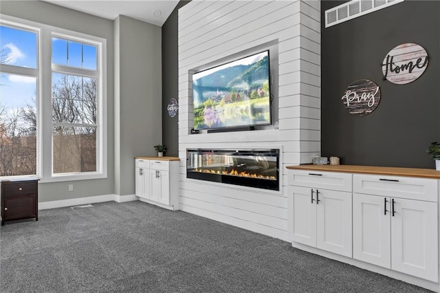 unfurnished living room featuring visible vents, a glass covered fireplace, carpet, wooden walls, and baseboards