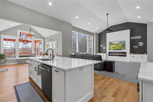 kitchen with dishwasher, light stone counters, a glass covered fireplace, white cabinetry, and a sink