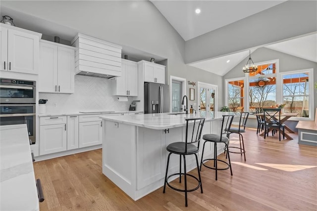 kitchen with a center island with sink, light stone counters, appliances with stainless steel finishes, white cabinets, and a sink