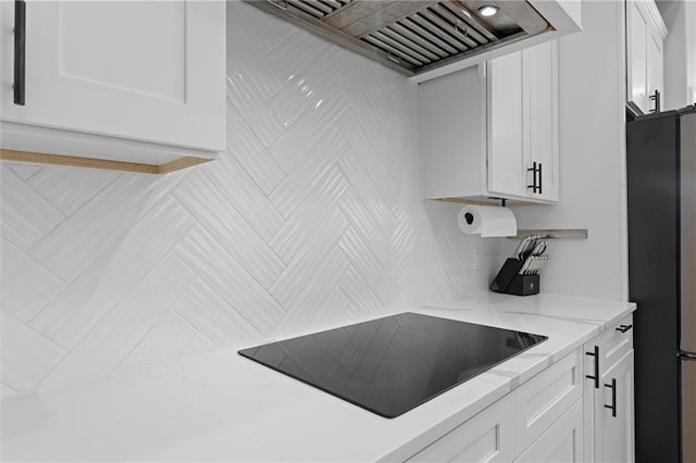 kitchen with light stone counters, freestanding refrigerator, custom range hood, white cabinetry, and black electric stovetop