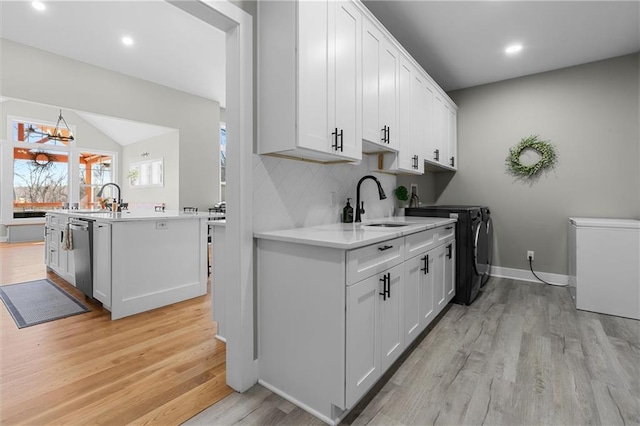 clothes washing area featuring light wood finished floors, laundry area, recessed lighting, separate washer and dryer, and a sink