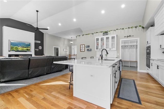 kitchen featuring a center island with sink, a sink, open floor plan, white cabinets, and light countertops