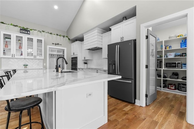 kitchen with light stone counters, lofted ceiling, a sink, black appliances, and white cabinetry