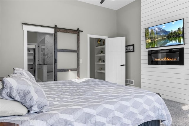 bedroom featuring visible vents, carpet, a barn door, and a glass covered fireplace