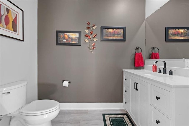 bathroom featuring baseboards, toilet, wood finished floors, and vanity