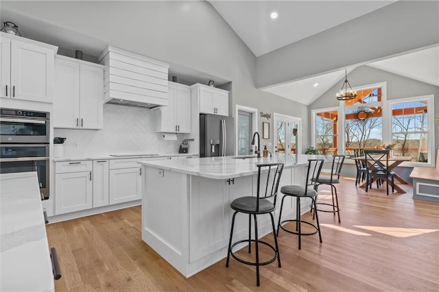 13723 Raliegh Ln, Holt, MO 64048 - kitchen with appliances with stainless steel finishes, white cabinetry, premium range hood, light stone countertops, and a kitchen island with sink
