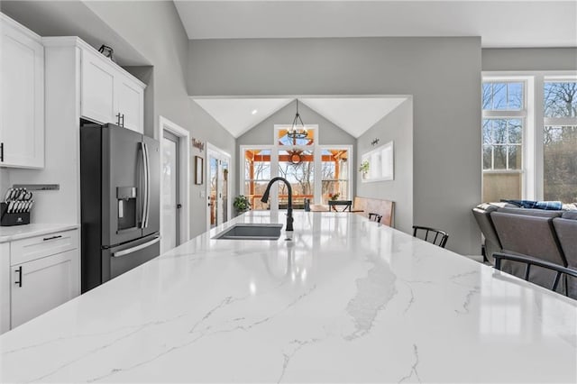 13723 Raliegh Ln, Holt, MO 64048 - kitchen with stainless steel fridge, open floor plan, white cabinets, light stone counters, and vaulted ceiling