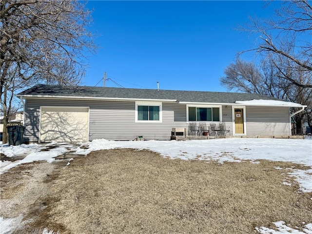 snow covered house featuring an attached garage and roof with shingles