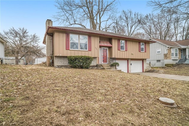 bi-level home featuring a garage, brick siding, concrete driveway, board and batten siding, and a chimney