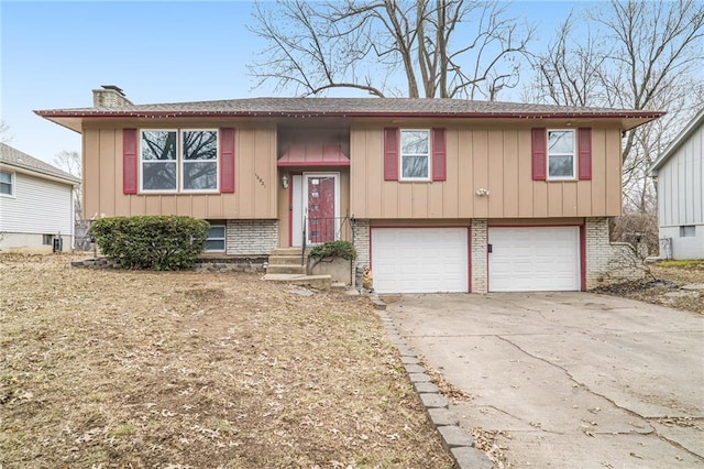 split foyer home with brick siding, a chimney, concrete driveway, board and batten siding, and a garage