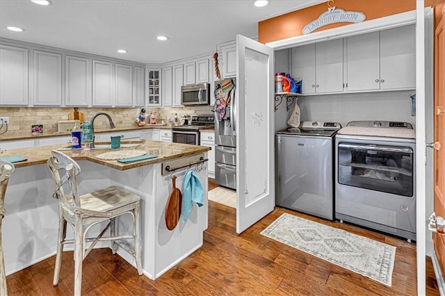 kitchen featuring stainless steel appliances, a sink, light stone countertops, washer and clothes dryer, and glass insert cabinets