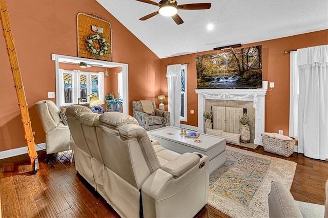 living room featuring high vaulted ceiling, dark wood-type flooring, a ceiling fan, baseboards, and a tiled fireplace