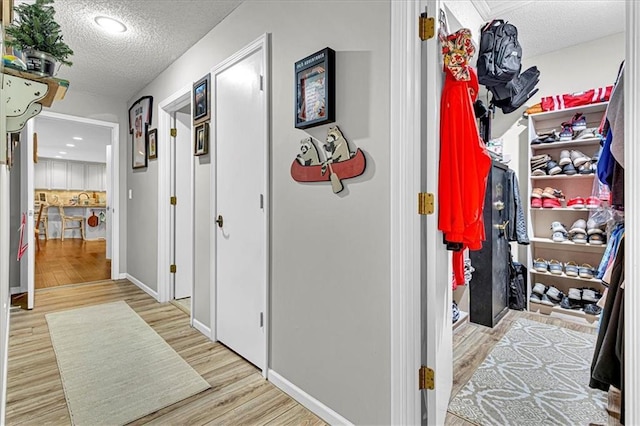 hallway with a textured ceiling, baseboards, and light wood-style floors