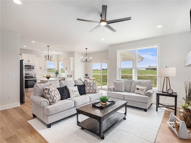 living area with recessed lighting, light wood-style flooring, baseboards, and ceiling fan with notable chandelier