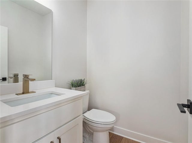 bathroom with toilet, baseboards, wood finished floors, and vanity