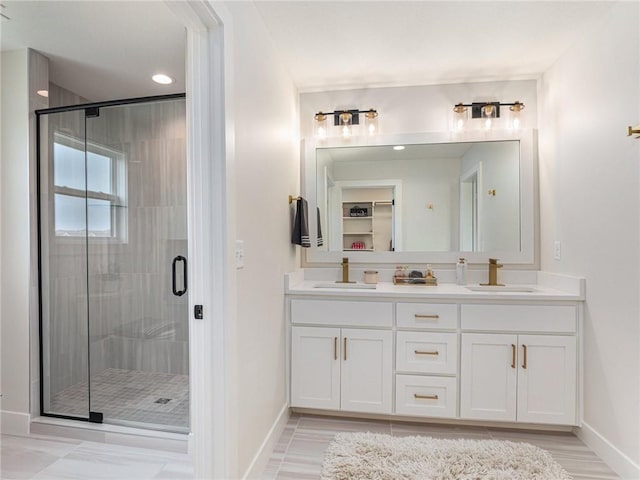 bathroom with double vanity, a stall shower, a sink, and baseboards