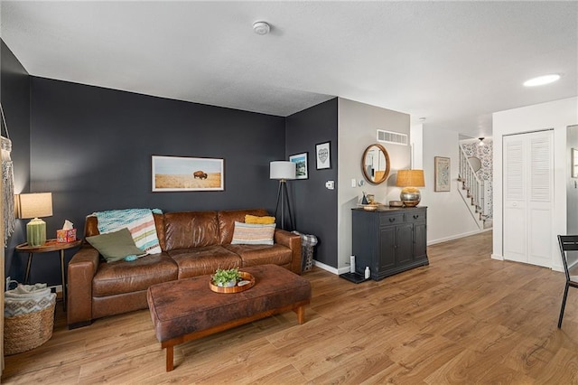 living room with light wood-style floors, visible vents, baseboards, and stairs