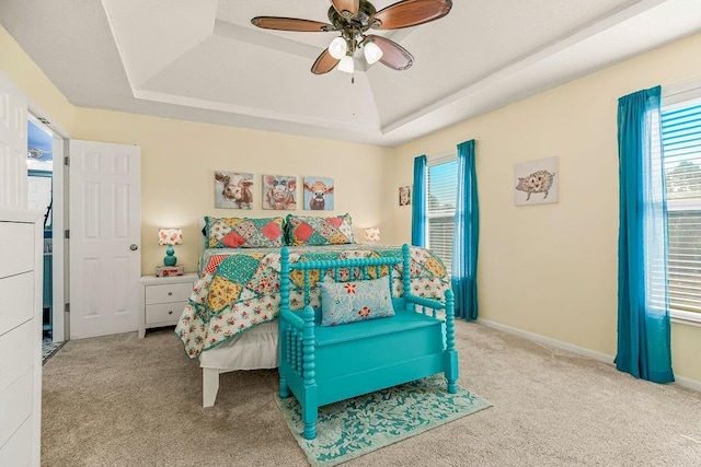 carpeted bedroom with baseboards, a raised ceiling, and a ceiling fan