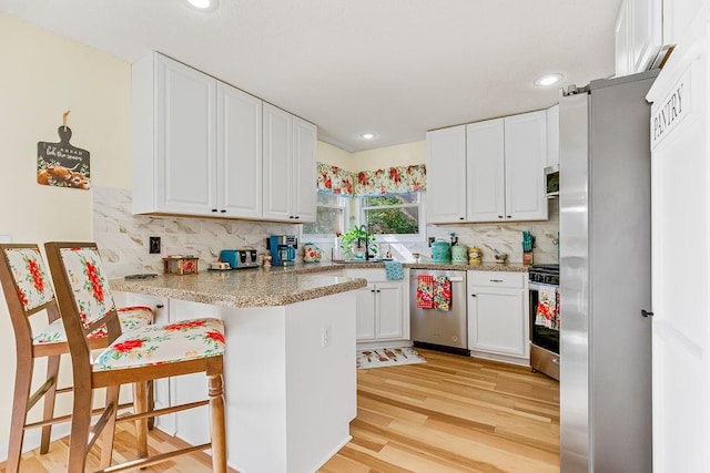 kitchen featuring a peninsula, white cabinetry, light wood-style floors, appliances with stainless steel finishes, and tasteful backsplash