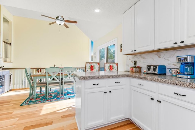 kitchen with light wood finished floors, lofted ceiling, decorative backsplash, white cabinetry, and a peninsula