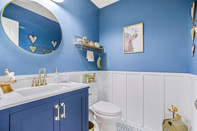 bathroom with a wainscoted wall, vanity, toilet, and a decorative wall