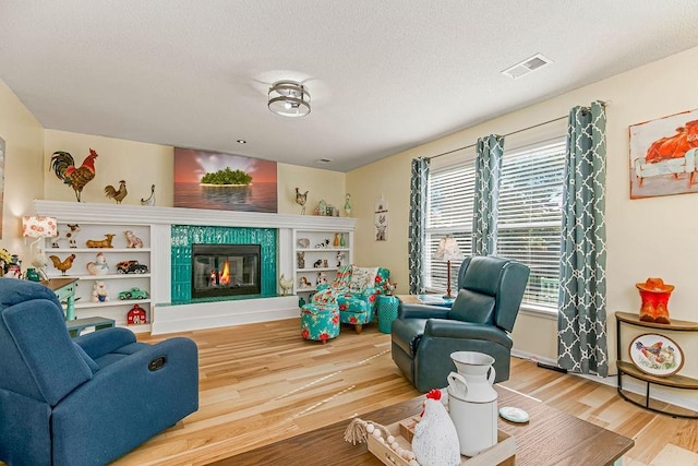 living room with a textured ceiling, a tile fireplace, wood finished floors, and visible vents