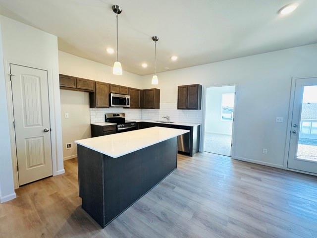 kitchen featuring tasteful backsplash, a center island, stainless steel appliances, light countertops, and pendant lighting