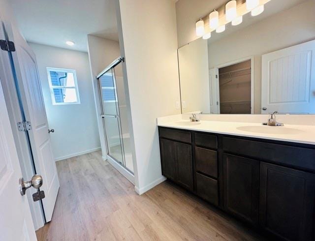 bathroom featuring double vanity, wood finished floors, a sink, and a shower stall