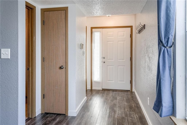 entryway featuring a textured ceiling, a textured wall, dark wood finished floors, and baseboards