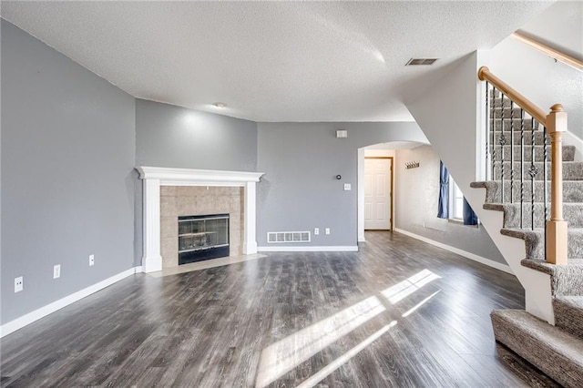 unfurnished living room featuring a textured ceiling, a fireplace, wood finished floors, visible vents, and stairway