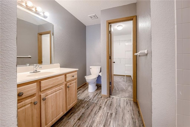 bathroom with baseboards, a textured wall, toilet, wood finished floors, and vanity