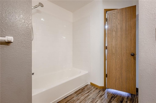 bathroom featuring a textured wall, bathing tub / shower combination, and wood finished floors