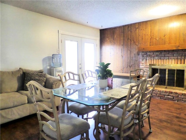 dining room featuring wood finished floors, french doors, wood walls, a textured ceiling, and a brick fireplace