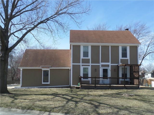 view of front of house featuring a deck, a front lawn, and roof with shingles