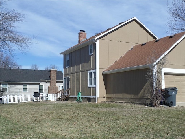 back of house with a yard, fence, a garage, and a chimney